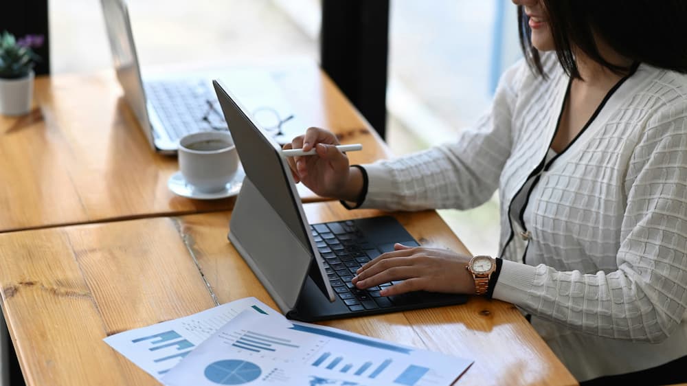 Woman working on a tablet in a modern office environment, with charts and notes on the desk.