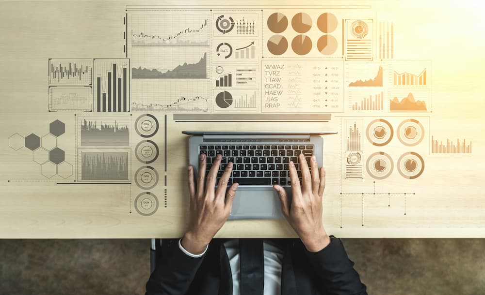 Hands of a professional typing on a laptop on a desk with charts and analytical data