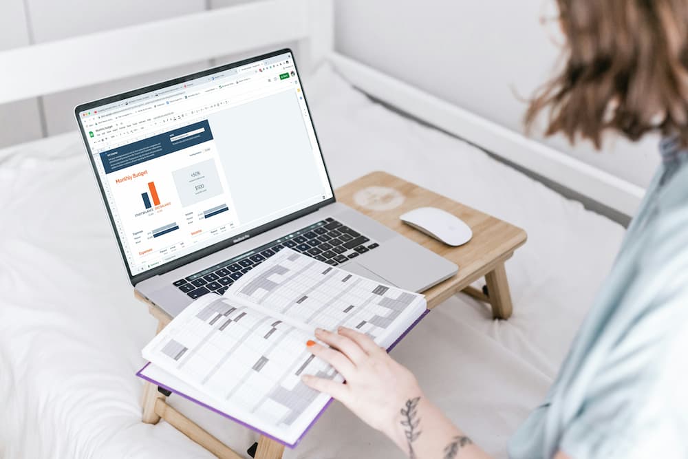A person working on a laptop that displays a spreadsheet titled 'Monthly Budget,' surrounded by charts and graphs. The individual is also referencing an open planner, highlighting the concept of centralized data management by combining digital tools and personal organization methods.