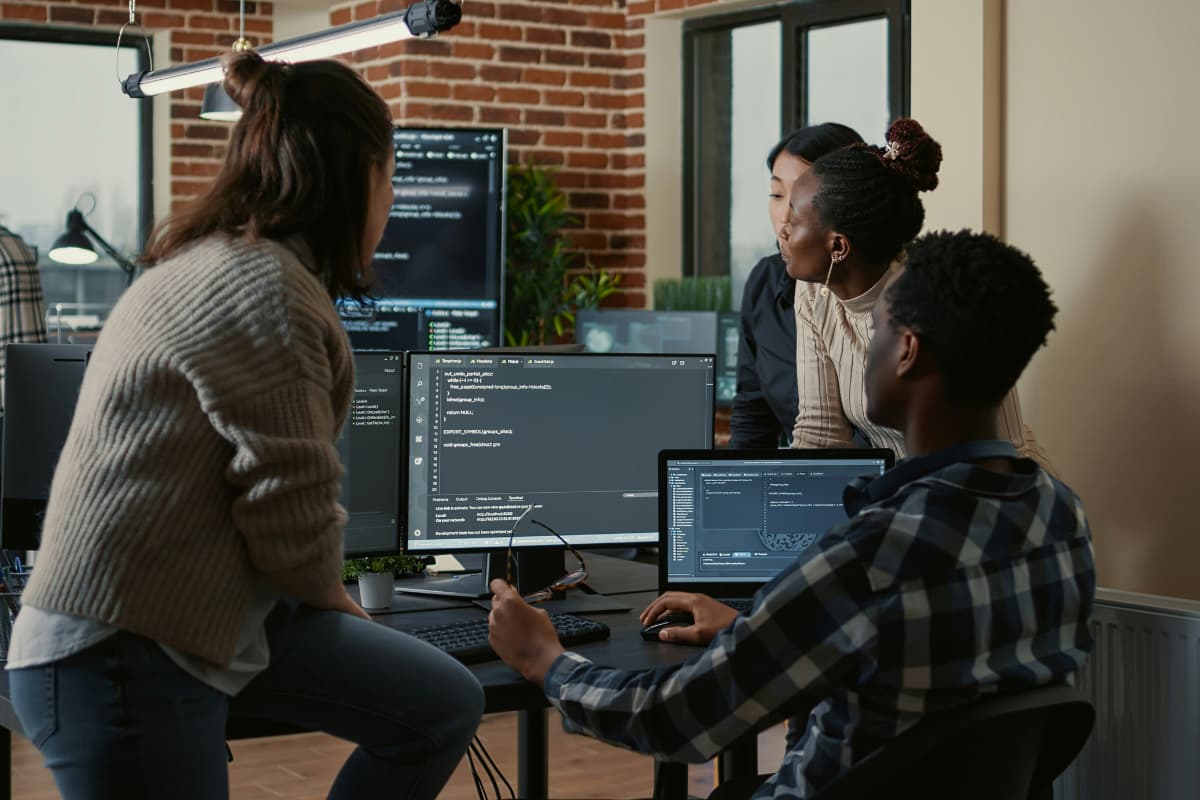 Team discussing custom software ROI while reviewing code on multiple computer screens in a modern office.
