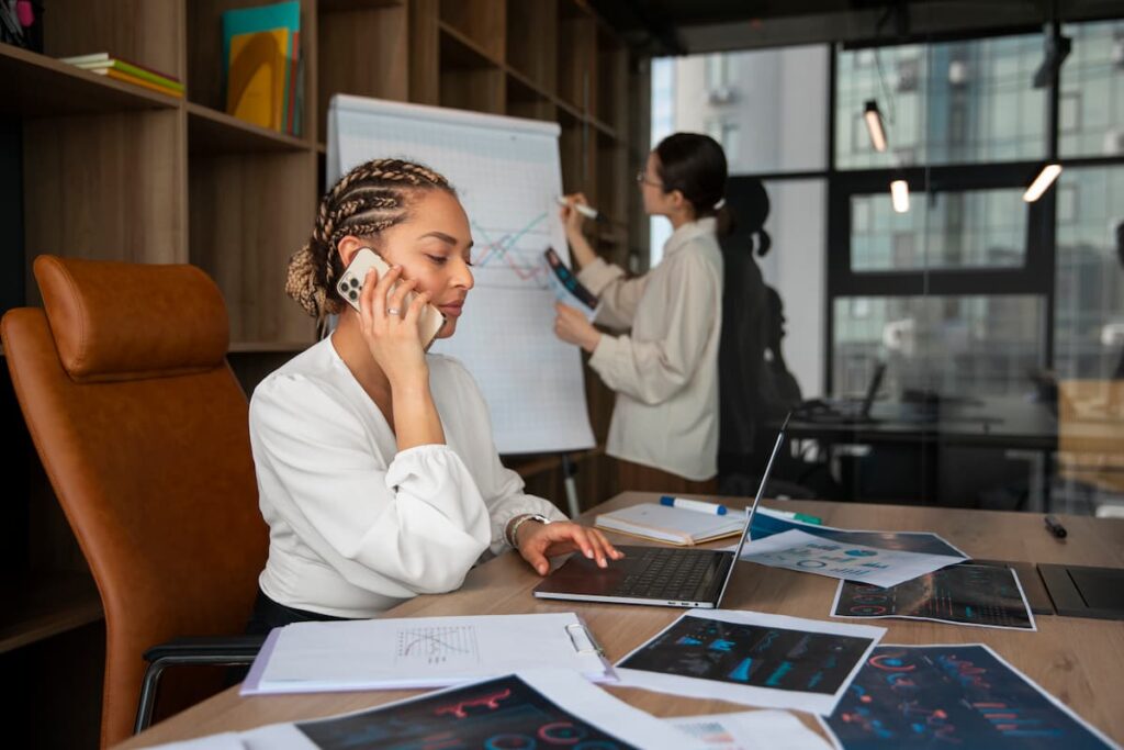 Two businesswomen analyzing charts and graphs in an office, breaking down data silos through teamwork and communication.