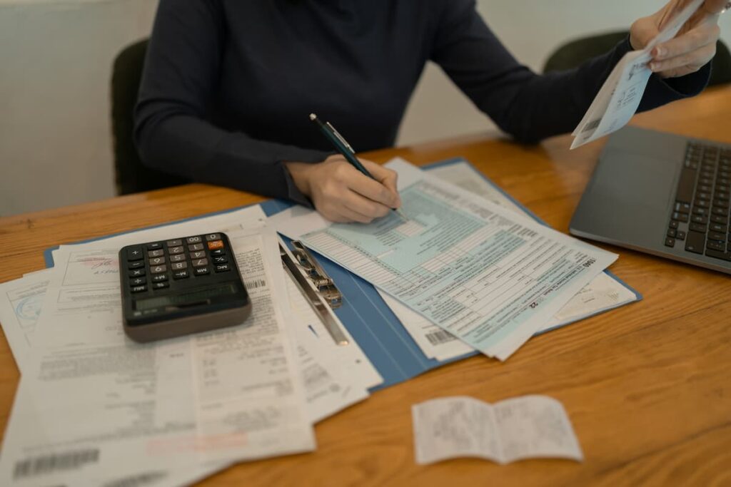 Person organizing receipts, forms, and using a calculator, illustrating how to improve financial reporting processes efficiently.