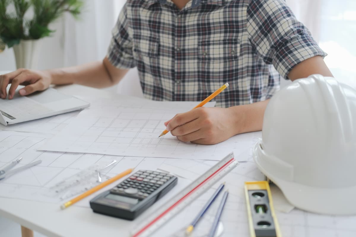 Engineer using calculator and blueprints to analyze how to manage production costs in manufacturing efficiently.