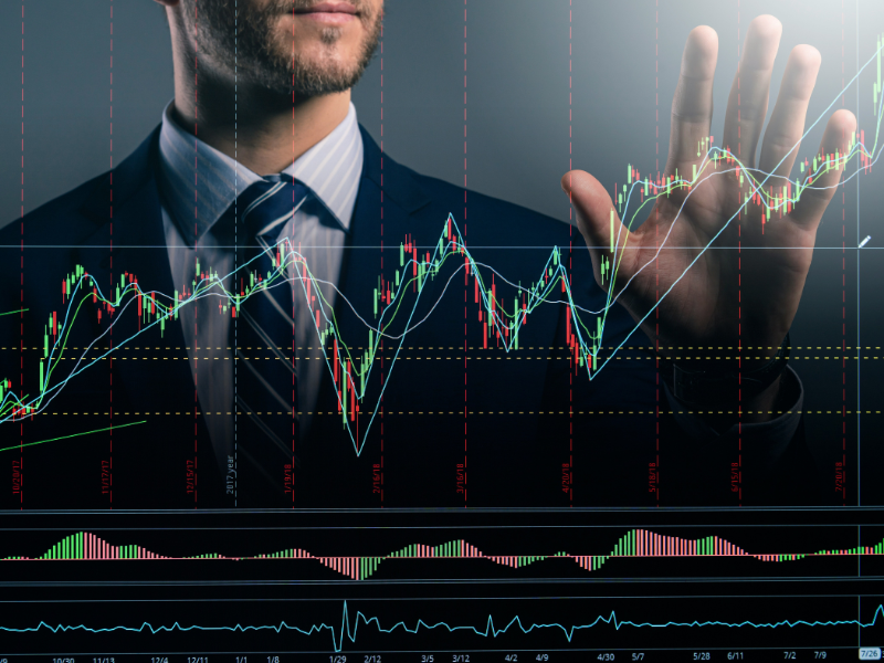 This image portrays a business professional in a suit interacting with a transparent financial interface, which displays complex stock market charts, technical indicators, and trend lines.